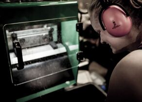 Mitarbeiterin beim Bedienen einer Maschine mit Gehörschutz