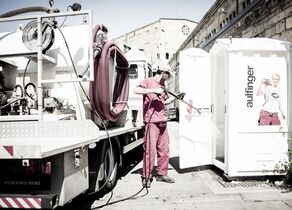 Mitarbeiter beim Säubern einer transportierbaren Toilette mit einem Hochdruckreiniger