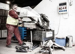 Mitarbeiter in Rot mit Warnweste legt dicke Kupferkabel in Schneidemaschine