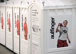 Weiße Toilettenkabinen mit Informationen zur Jörg Aulfinger GmbH & Co.KG und Bildern von Mitarbeitern beklebt